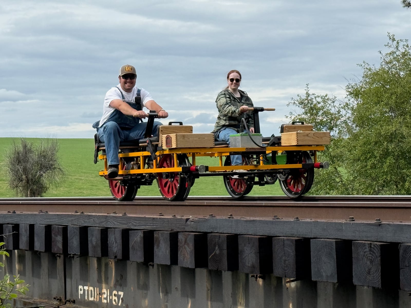 Two riders seated on a yellow handcar on railroad tracks